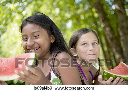 Stock Photo - Friends eating watermelon in garden. Fotosearch