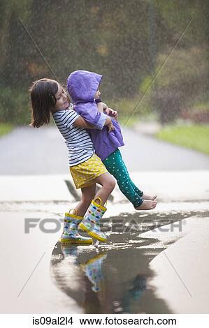 Picture - Girl carrying toddler sister through puddle on street. Fotosearch