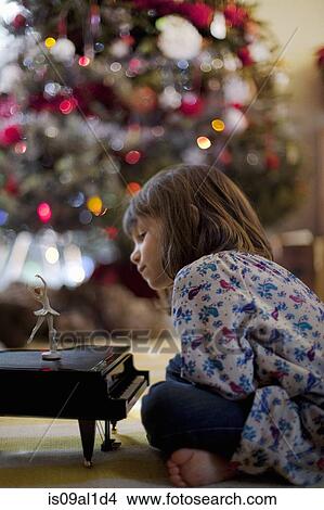 Girl sitting on living room floor listening to toy piano music box at Xmas View Large Photo Image Picture - Girl sitting on living room floor listening to toy piano music box at Xmas. Fotosearch