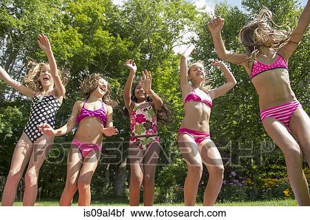 Stock Image - Girls in swimming costume jumping in garden. Fotosearch