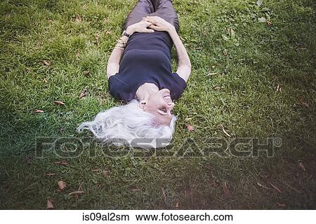 Picture - Gray haired woman taking break and enjoying grass in city park. Fotosearch