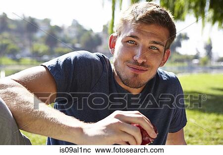 Stock Image - Man eating apple in park. Fotosearch