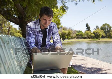 Man using laptop on park bench View Large Photo Image Stock Photograph - Man using laptop on park bench. Fotosearch