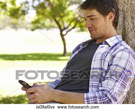 Stock Photograph - Man using smartphone in park. Fotosearch