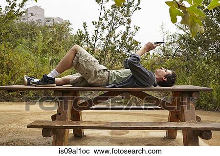 Stock Image - Man using smartphone on table in park. Fotosearch