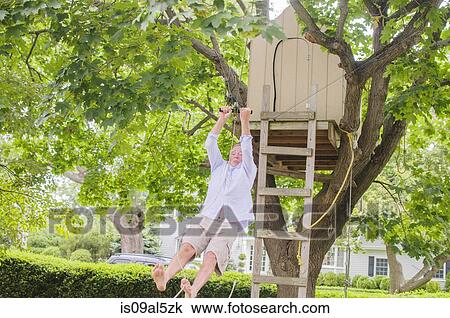 Stock Image - Mature man sliding down on pulley from tree house. Fotosearch
