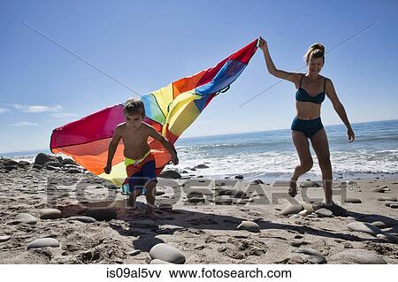 Stock Photo - Mature woman and son running with multi colored textile on beach, County Park, Los Angeles, California, USA. Fotosearch