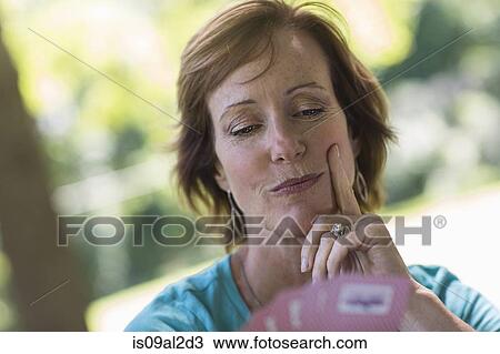 Stock Image - Mature woman looking at hand of playing cards. Fotosearch