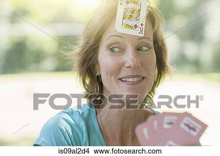 Picture - Mature woman playing cards, a playing card stuck on her forehead. Fotosearch