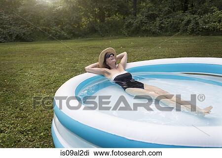 Stock Image - Mature woman relaxing in paddling pool. Fotosearch