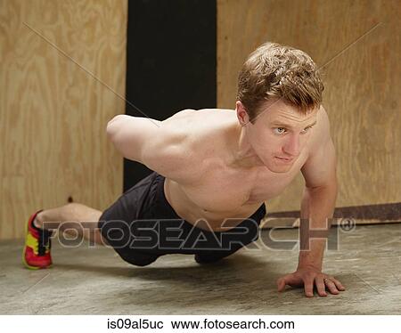 Stock Image - Mid adult male doing one armed push ups in gym. Fotosearch