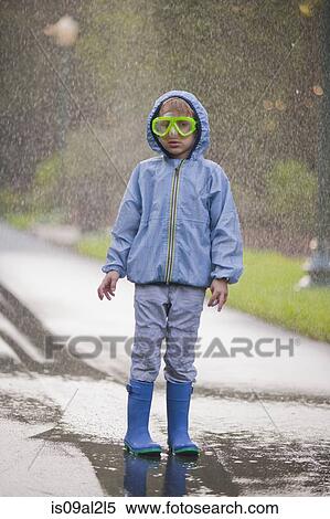 Stock Photography - Portrait of boy wearing scuba goggles and rubber boots standing in street puddle. Fotosearch