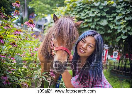 Stock Image - Portrait of teenage girl standing with pony, outdoors. Fotosearch