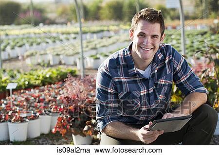 Stock Image - Portrait of young male worker using digital tablet in plant nursery polytunnel. Fotosearch
