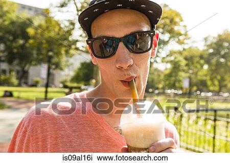 Stock Image - Portrait of young man drinking frappe in park. Fotosearch