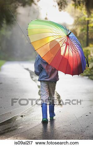 Stock Photo - Rear view of boy carrying umbrella on street. Fotosearch