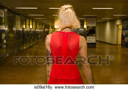Stock Photo - Rear view of young woman wearing red dress in subway station. Fotosearch