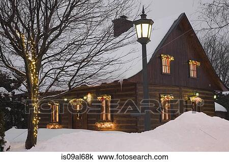 Stock Image - Reconstructed 1840s residential log home with Christmas decorations at dusk, Quebec, Canada. Fotosearch
