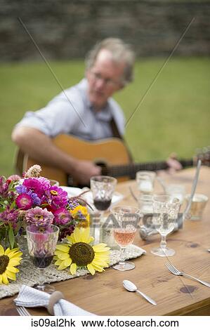 Stock Image - Table with half finished drinks, mature man playing guitar in background. Fotosearch