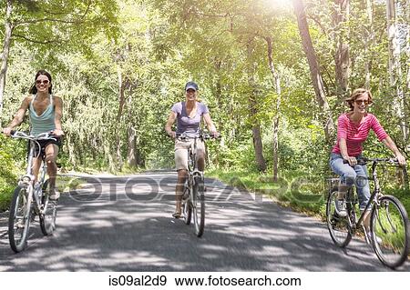 Stock Photo - Three mature woman riding bicycles along country road. Fotosearch