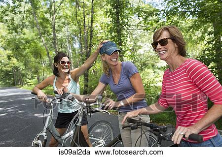Stock Image - Three mature woman with bicycles along country road. Fotosearch
