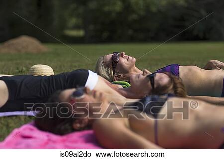 Picture - Three mature women in swimwear, sunbathing on grass. Fotosearch