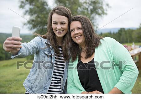 Two female friends taking self portrait using smartphone, outdoors View Large Photo Image Stock Image - Two female friends taking self portrait using smartphone, outdoors. Fotosearch
