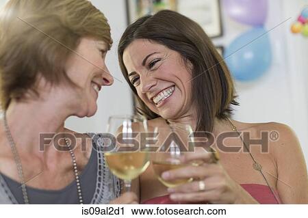 Stock Image - Two mature women, drinking wine and laughing. Fotosearch