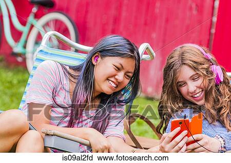 Stock Image - Two teenagers wearing headphones, listening to music, outdoors. Fotosearch