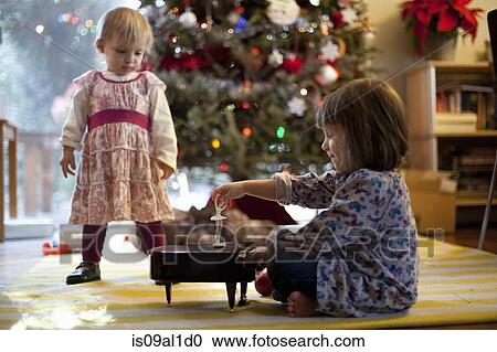 Stock Image - Two young sisters listening to toy piano music box at Xmas. Fotosearch