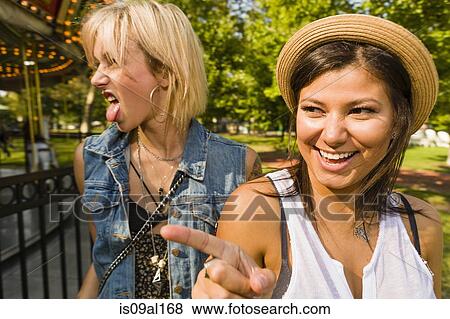 Stock Photo - Two young women pointing and sticking out tongue in park. Fotosearch