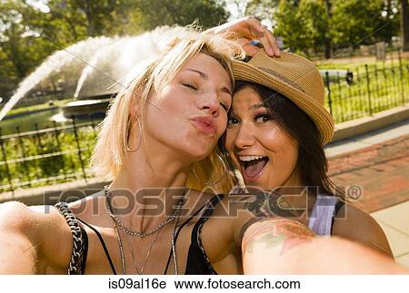 Stock Image - Two young women taking selfie in park. Fotosearch