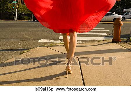 Stock Photography - Waist down shot of young woman strolling along sidewalk wearing flowing red skirt. Fotosearch