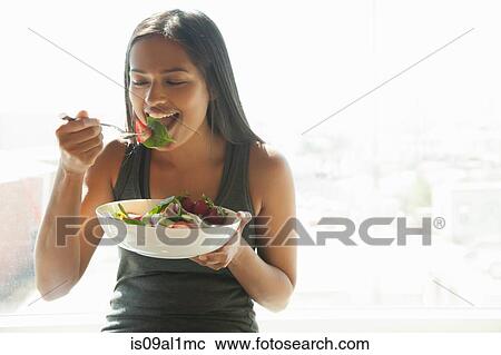Stock Image - Woman eating salad at home. Fotosearch