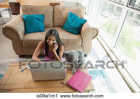 Stock Image - Woman on smartphone using laptop at home. Fotosearch