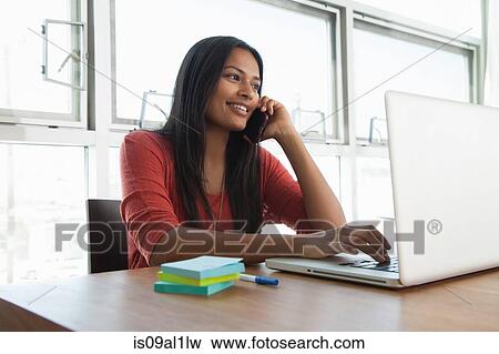 Woman on smartphone using laptop at home View Large Photo Image Stock Photo - Woman on smartphone using laptop at home. Fotosearch