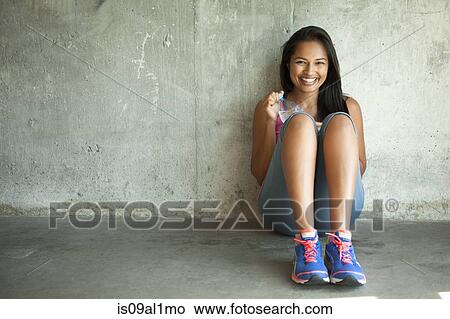 Picture - Woman with water bottle sitting against wall. Fotosearch