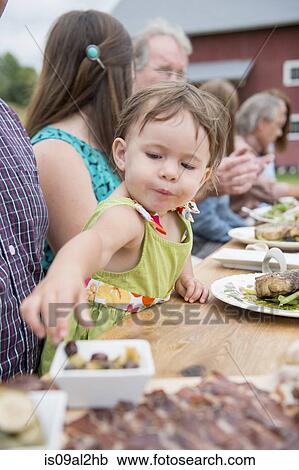 Stock Image - Young child picking olive from dish at family meal, outdoors. Fotosearch