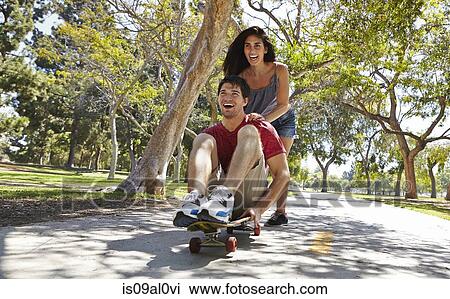 Stock Image - Young couple skateboarding in park. Fotosearch