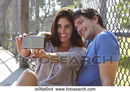 Stock Image - Young couple taking selfie by wire fence. Fotosearch