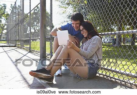 Stock Image - Young couple using digital tablet by wire fence. Fotosearch