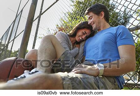 Stock Image - Young couple with basketball sitting by wire fence. Fotosearch