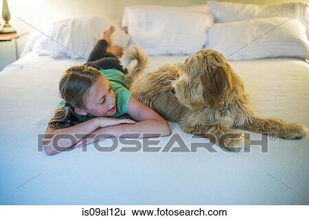 Young girl lying on bed next to dog View Large Photo Image Stock Photograph - Young girl lying on bed next to dog. Fotosearch