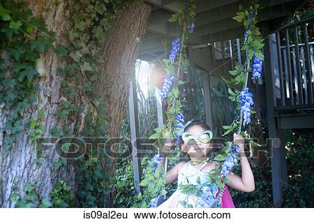 Stock Photograph - Young girl wearing fancy dress costume, sitting on tree swing. Fotosearch