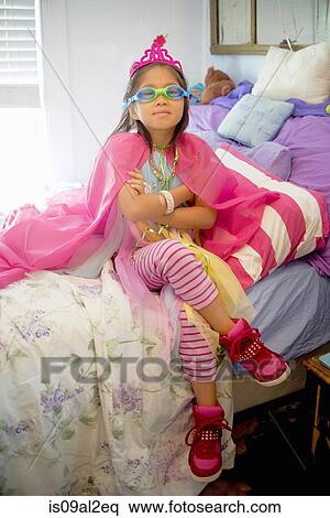 Stock Photography - Young girl wearing fancy dress costume, sitting on bed. Fotosearch