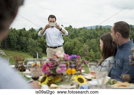 Young man taking photograph of family during meal, outdoors View Large Photo Image Picture - Young man taking photograph of family during meal, outdoors. Fotosearch