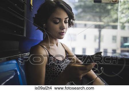 Young woman commuting on bus listening to music on smartphone, New York, US View Large Photo Image Picture - Young woman commuting on bus listening to music on smartphone, New York, US. Fotosearch