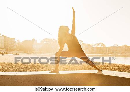 Stock Photo - Young woman doing yoga on pier at Pacific beach at sunset, San Diego, California, USA. Fotosearch