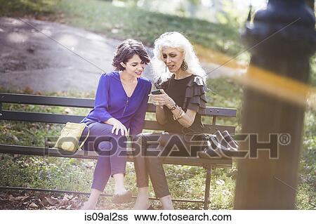 Young woman in city park with mentor looking at photos in smartphone View Large Photo Image Stock Photograph - Young woman in city park with mentor looking at photos in smartphone. Fotosearch