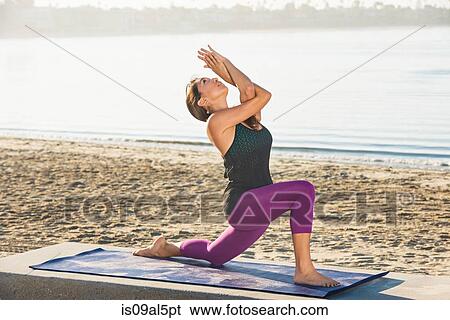 Stock Photograph - Young woman kneeling doing yoga on pier at Pacific beach, San Diego, California, USA. Fotosearch